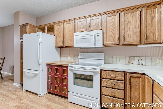 kitchen with brown cabinets, light countertops, light wood-style floors, a textured ceiling, and white appliances