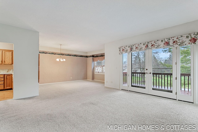 unfurnished living room featuring light carpet, an inviting chandelier, baseboards, and french doors