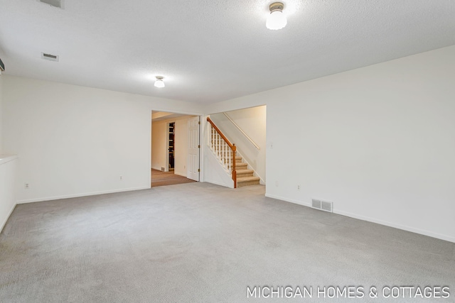 spare room with stairway, carpet, visible vents, and a textured ceiling