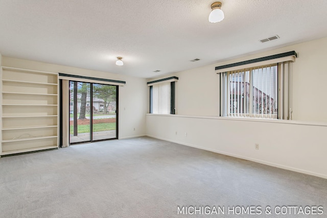 spare room featuring carpet floors, baseboards, visible vents, and a textured ceiling