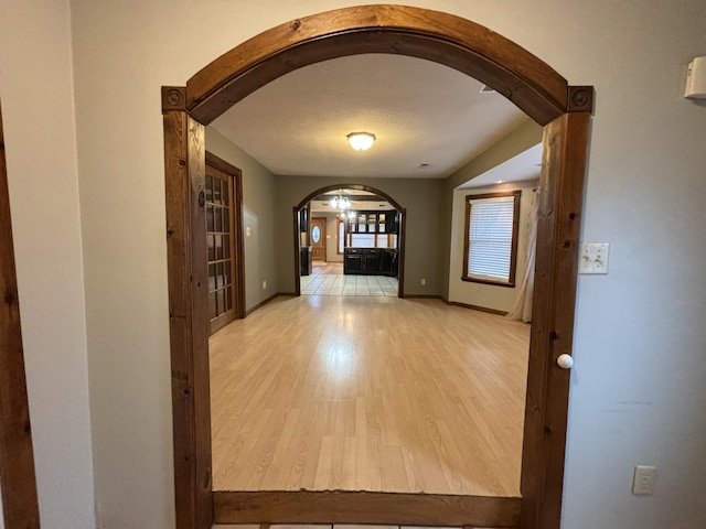 hallway featuring light wood finished floors, baseboards, and arched walkways