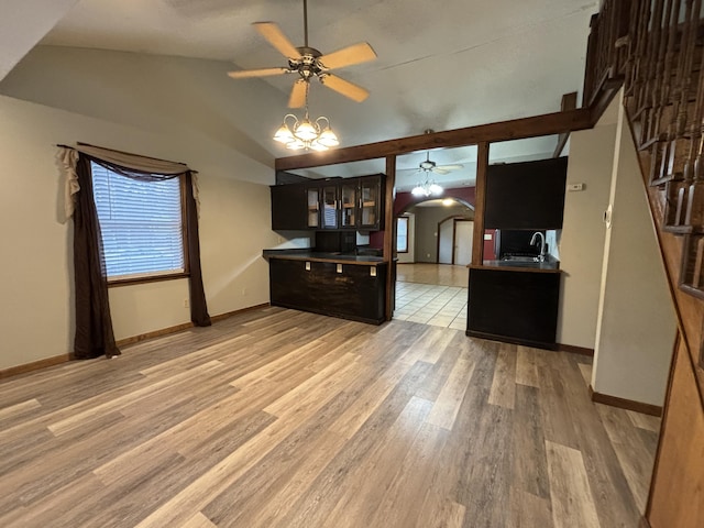 kitchen featuring arched walkways, ceiling fan with notable chandelier, a sink, vaulted ceiling, and light wood-type flooring