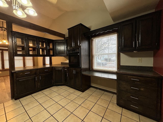 kitchen featuring light tile patterned floors, oven, vaulted ceiling, built in desk, and dark countertops