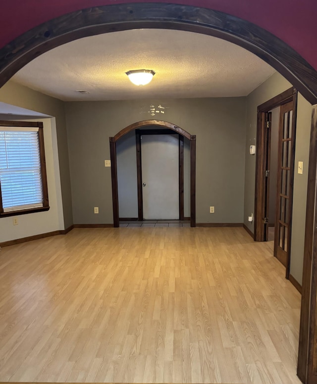 unfurnished room with arched walkways, a textured ceiling, light wood-style flooring, and baseboards