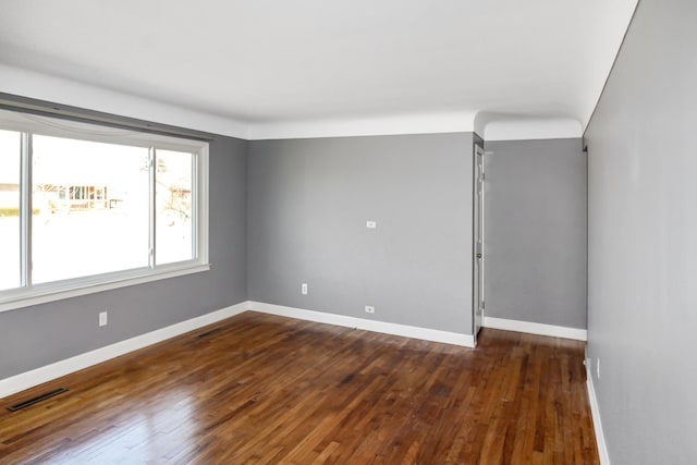 spare room with baseboards, visible vents, and dark wood-style flooring