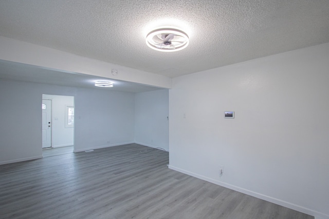 unfurnished room with a textured ceiling, baseboards, and wood finished floors