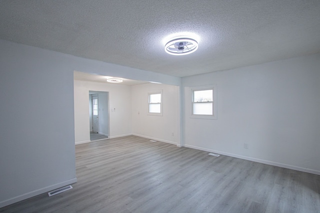 spare room featuring baseboards, a textured ceiling, visible vents, and wood finished floors