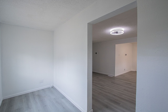 empty room featuring a textured ceiling, wood finished floors, and baseboards