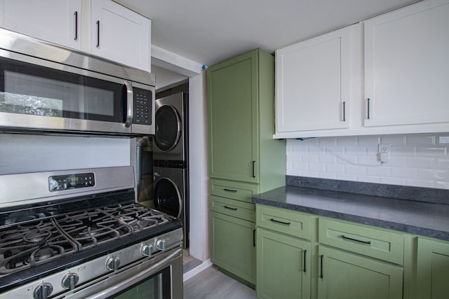 kitchen featuring tasteful backsplash, dark countertops, appliances with stainless steel finishes, stacked washing maching and dryer, and green cabinetry