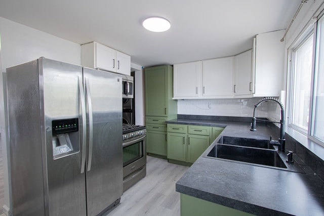 kitchen with stainless steel appliances, dark countertops, green cabinets, white cabinetry, and a sink