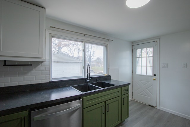 kitchen with green cabinetry, dishwasher, dark countertops, light wood-style floors, and a sink