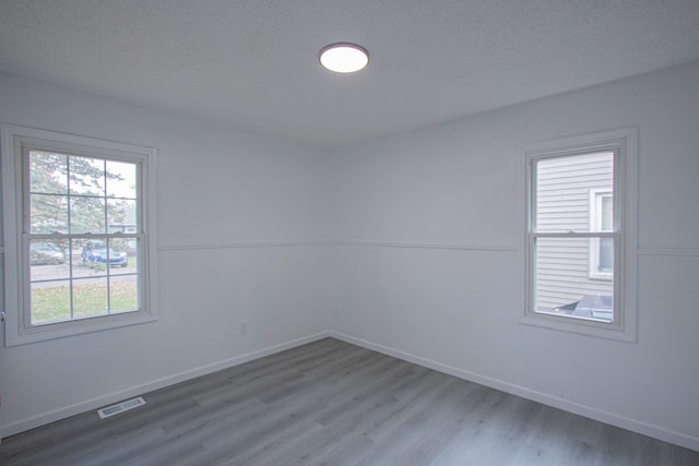 empty room featuring visible vents, a textured ceiling, baseboards, and wood finished floors