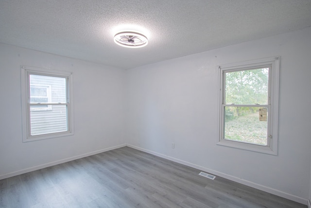 unfurnished room featuring visible vents, a textured ceiling, baseboards, and wood finished floors