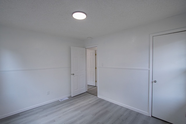 unfurnished bedroom with a textured ceiling, baseboards, and wood finished floors