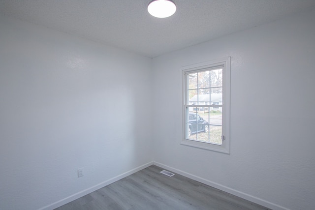 unfurnished room featuring visible vents, a textured ceiling, baseboards, and wood finished floors