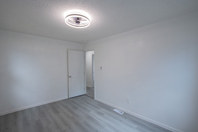 spare room featuring a textured ceiling, light wood finished floors, visible vents, and baseboards