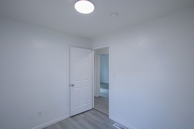 empty room with light wood finished floors, visible vents, and baseboards