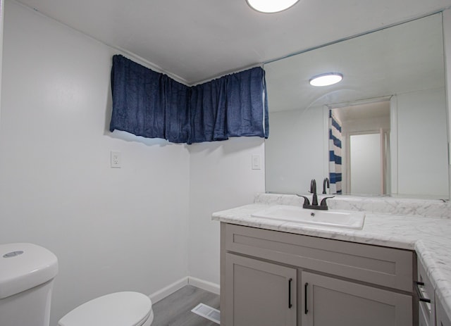 bathroom with toilet, wood finished floors, visible vents, vanity, and baseboards