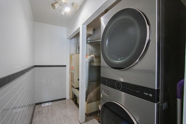 laundry room featuring stacked washer and dryer, laundry area, wainscoting, and tile walls