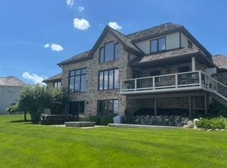 back of house with stone siding, a lawn, stairway, and a wooden deck