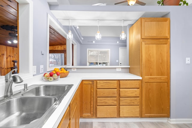 kitchen featuring a ceiling fan, a peninsula, a sink, light countertops, and decorative light fixtures