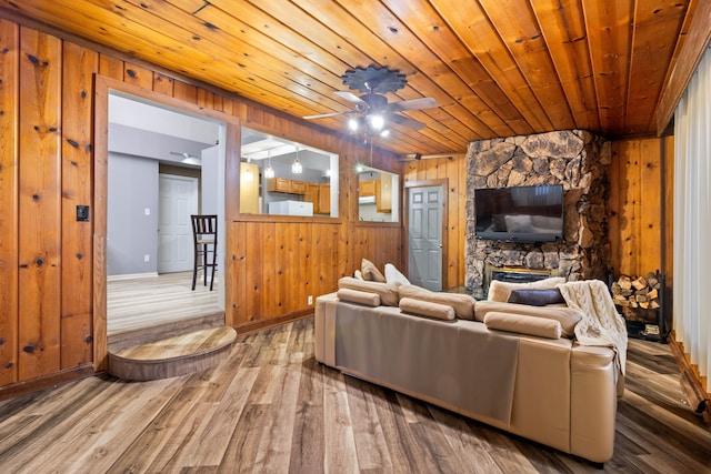 living area with wooden walls, baseboards, wood ceiling, a stone fireplace, and wood finished floors