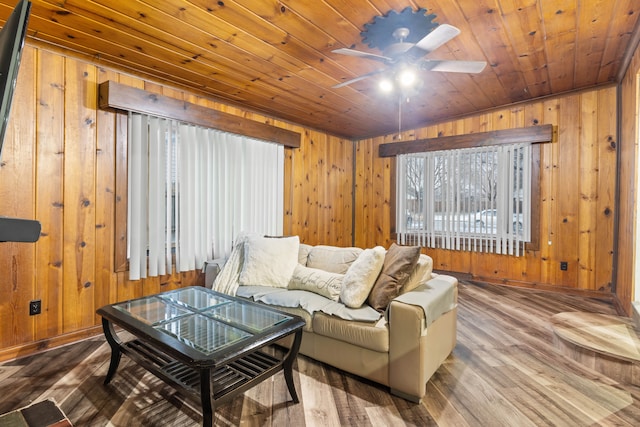 living area featuring wooden walls, wood finished floors, baseboards, ceiling fan, and wood ceiling