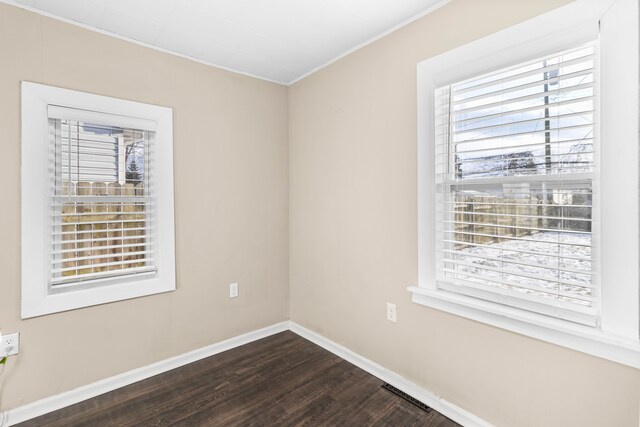 spare room with dark wood finished floors, visible vents, and baseboards