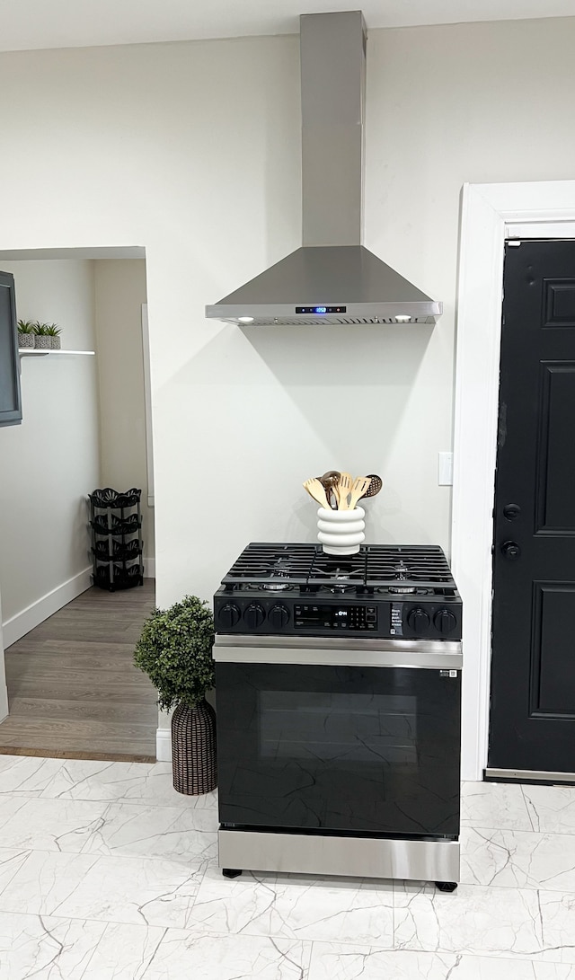 kitchen featuring black range with gas cooktop, marble finish floor, wall chimney exhaust hood, and baseboards