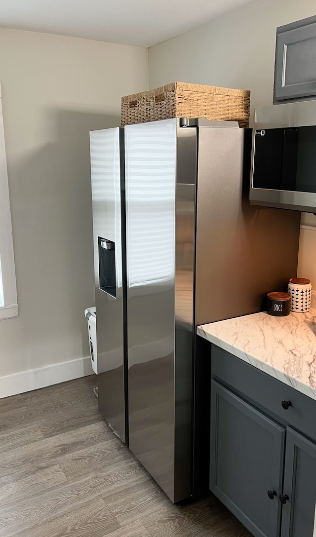 kitchen with light stone counters, baseboards, gray cabinets, light wood finished floors, and stainless steel microwave