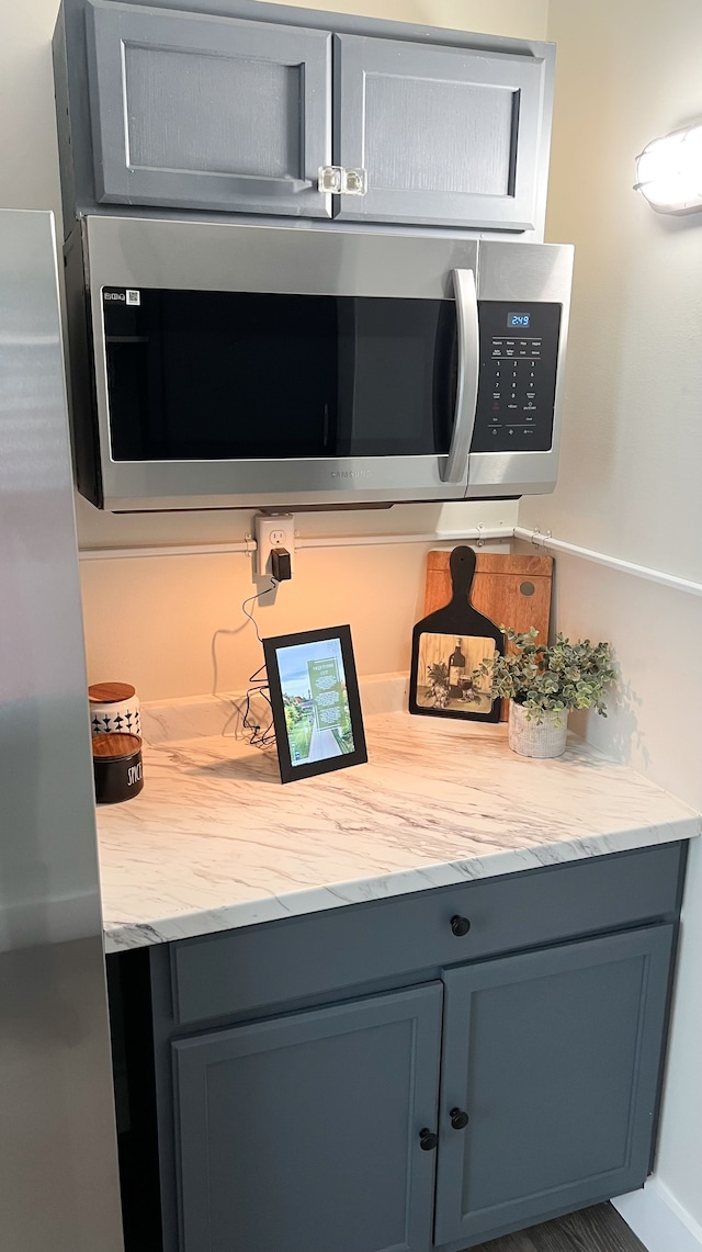 details with light stone countertops, stainless steel microwave, and gray cabinetry