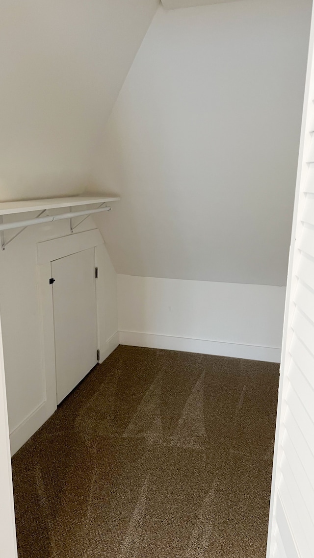 additional living space with vaulted ceiling, dark carpet, and baseboards