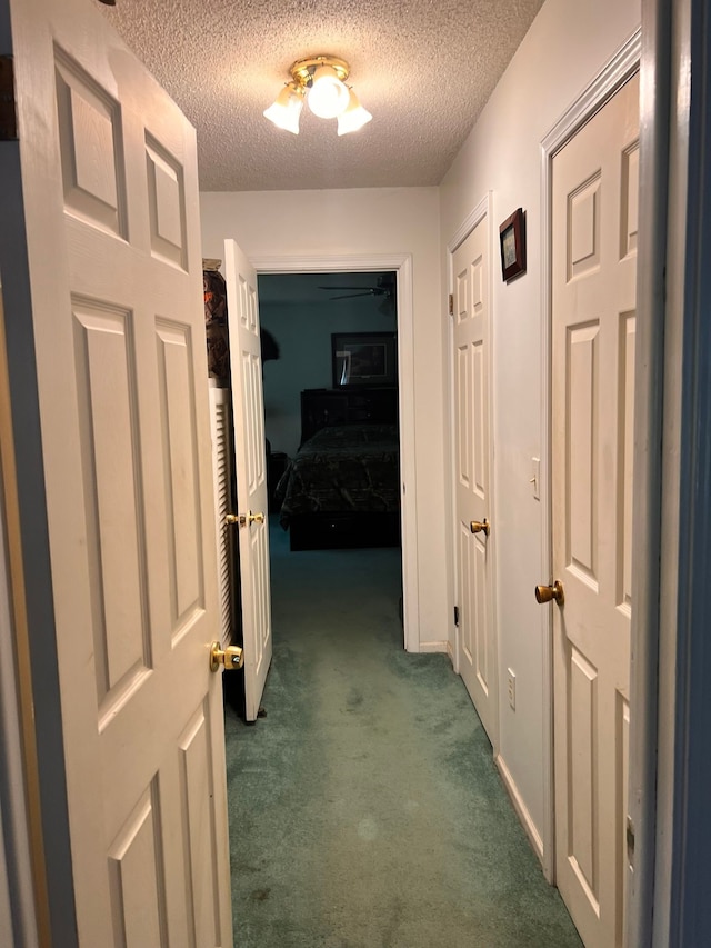 corridor featuring a textured ceiling and dark colored carpet