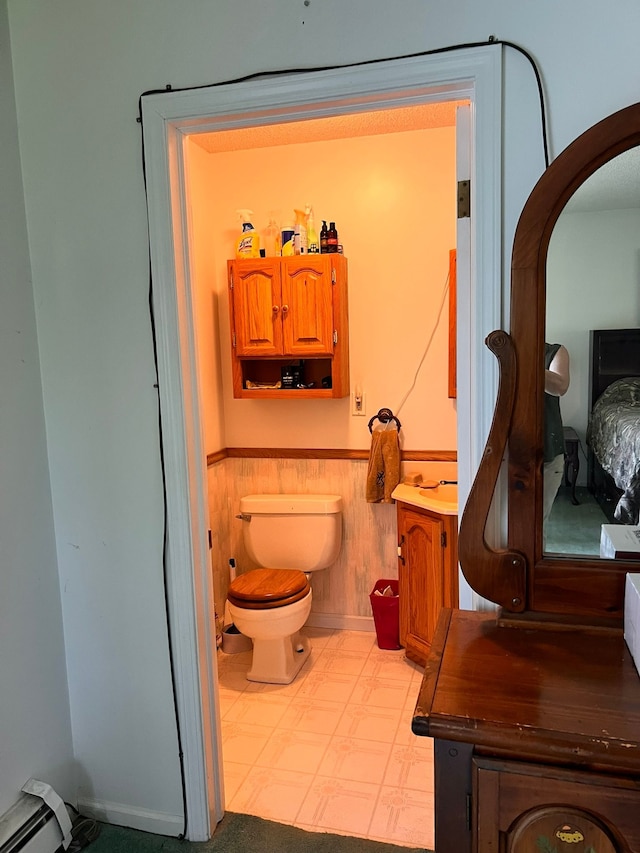 bathroom featuring a wainscoted wall, toilet, wood walls, and baseboard heating