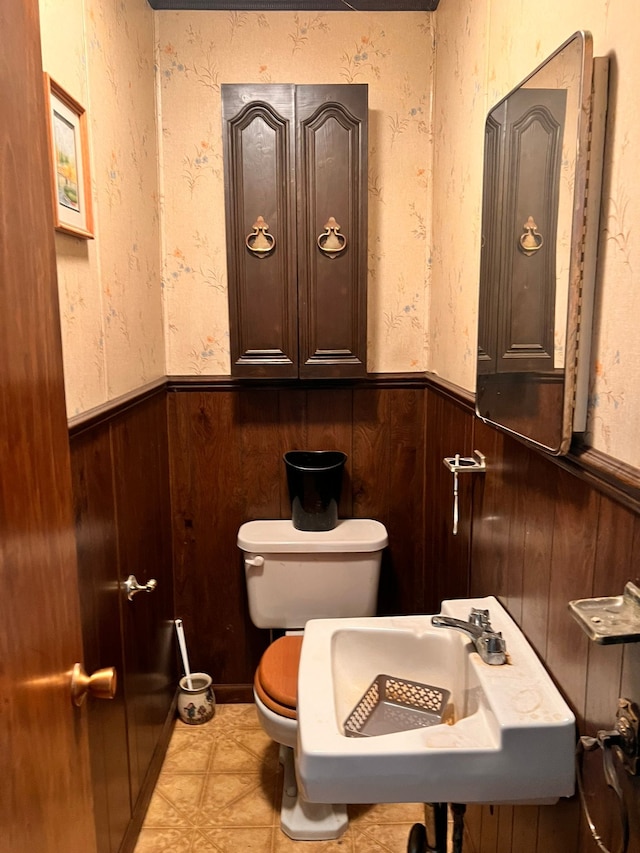 bathroom featuring wainscoting, a sink, wood walls, and toilet