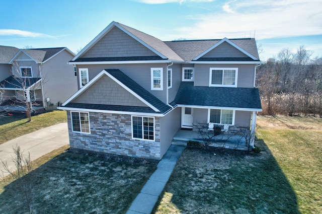 view of front of house with stone siding, a porch, a front yard, and roof with shingles