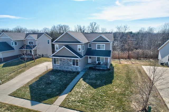 view of front of home featuring stone siding, roof with shingles, covered porch, and a front yard