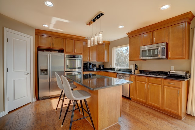 kitchen featuring a sink, a kitchen breakfast bar, a center island, appliances with stainless steel finishes, and light wood finished floors