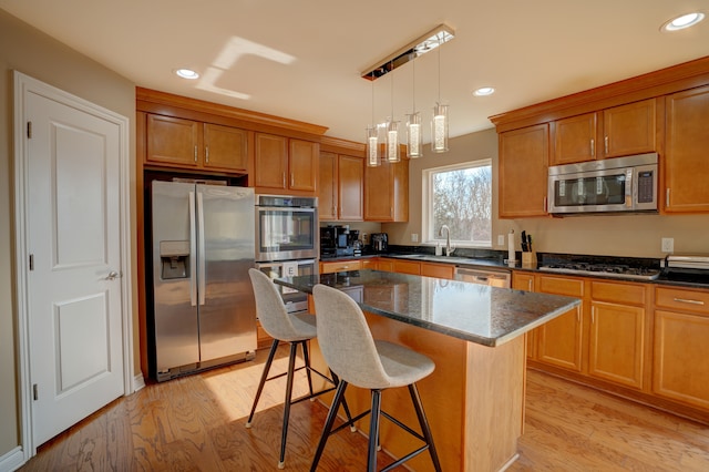 kitchen featuring brown cabinets, a breakfast bar, a sink, light wood-style floors, and appliances with stainless steel finishes