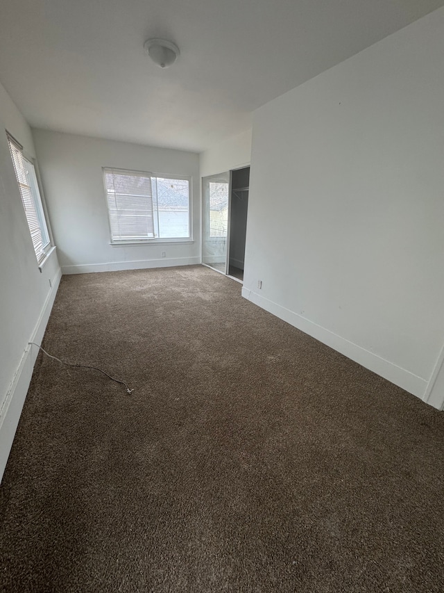 empty room with dark colored carpet, a wealth of natural light, and baseboards