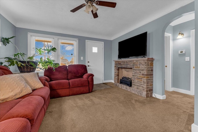 living room featuring baseboards, carpet, a fireplace, arched walkways, and a ceiling fan