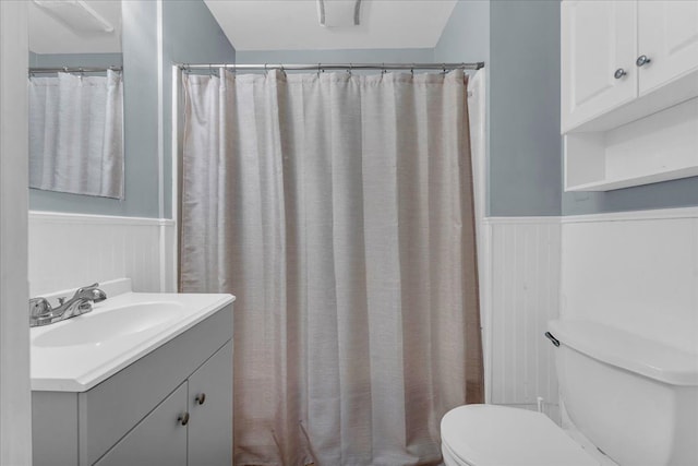 bathroom featuring vanity, curtained shower, toilet, and a wainscoted wall