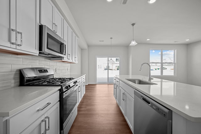 kitchen featuring tasteful backsplash, dark wood-style floors, appliances with stainless steel finishes, hanging light fixtures, and a sink