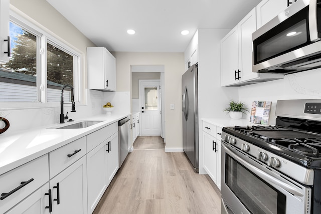 kitchen featuring light wood-style flooring, stainless steel appliances, light countertops, white cabinetry, and a sink