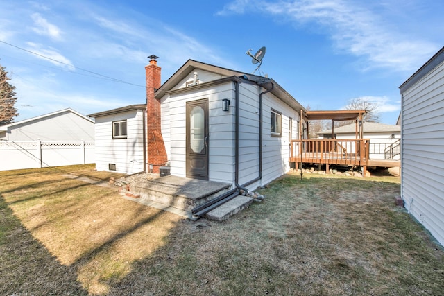 back of house featuring a lawn, a chimney, a wooden deck, and fence