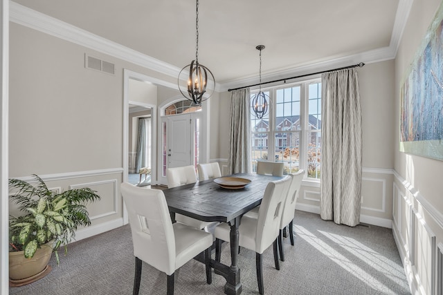 carpeted dining area featuring crown molding, a wainscoted wall, visible vents, and a decorative wall