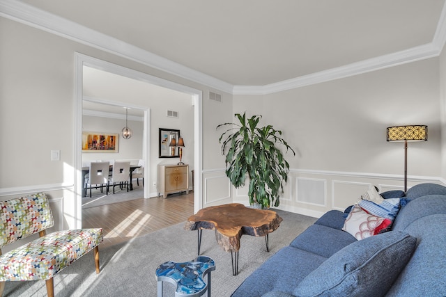 living room with visible vents, a decorative wall, crown molding, and wood finished floors