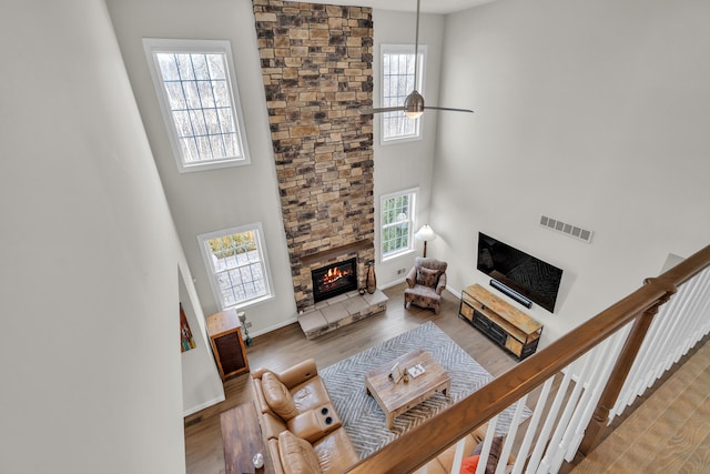 living area featuring a fireplace, wood finished floors, a towering ceiling, visible vents, and a ceiling fan