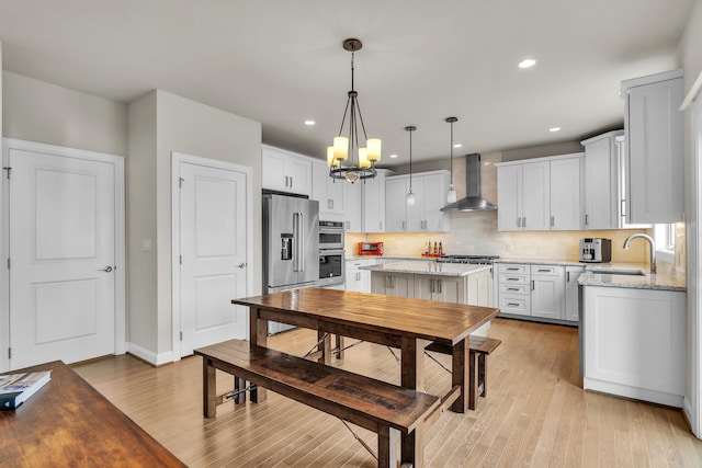 kitchen with stainless steel appliances, a sink, wall chimney range hood, light wood-type flooring, and decorative backsplash