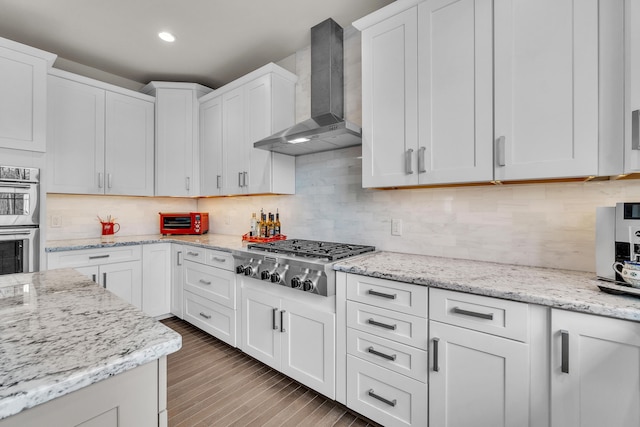 kitchen featuring decorative backsplash, appliances with stainless steel finishes, white cabinets, wood finished floors, and wall chimney exhaust hood